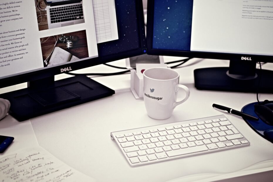 white ceramic mug between apple magic keyboard and two flat screen computer monitors