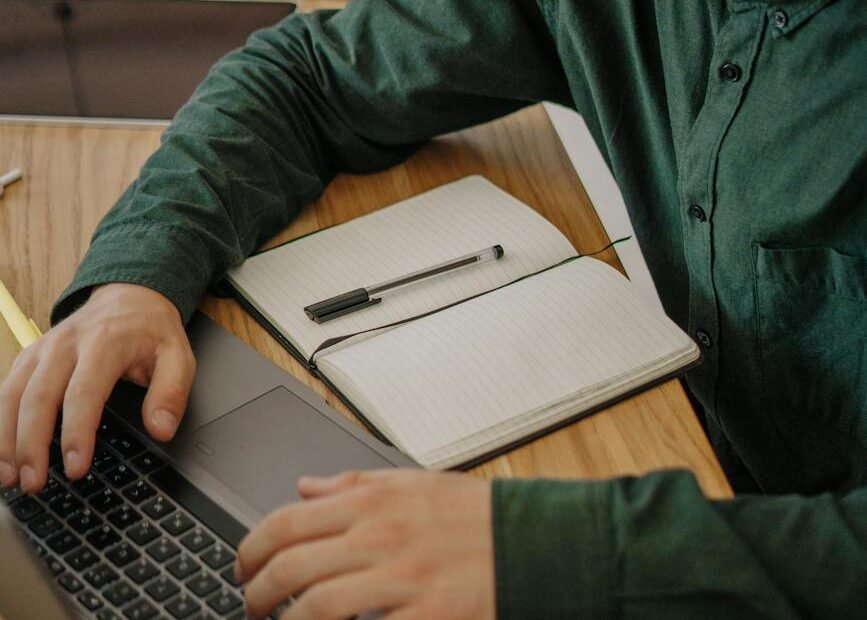 close up shot of a male student in green long sleeves using a laptop on a wooden desk