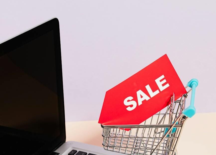 a red sale tag on a miniature shopping cart placed on a macbook laptop